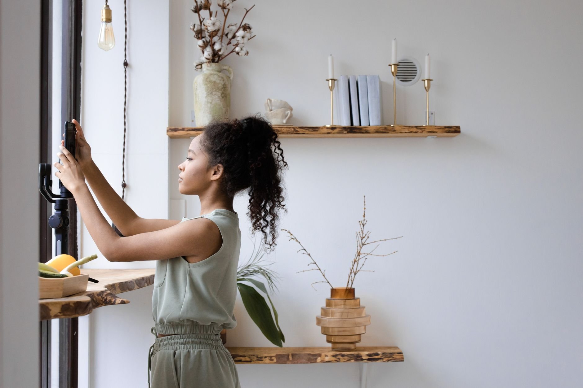 Side view of a young woman creating content with a smartphone indoors.